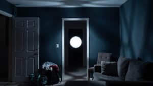 A white glowing orb floats from a dark hallway doorway toward the center of a dimly lit vacation rental at 2am