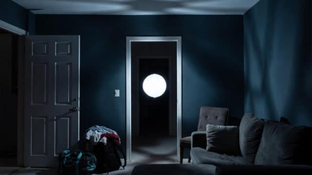 A white glowing orb floats from a dark hallway doorway toward the center of a dimly lit vacation rental at 2am