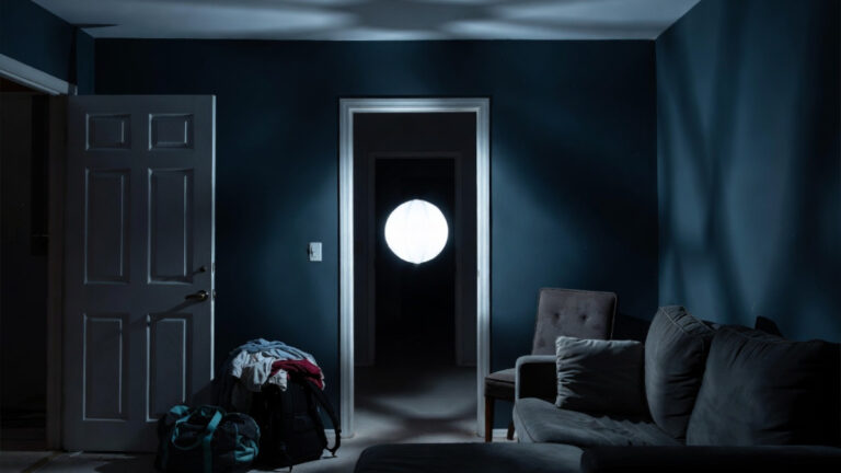 A white glowing orb floats from a dark hallway doorway toward the center of a dimly lit vacation rental at 2am