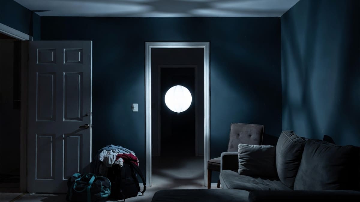 A white glowing orb floats from a dark hallway doorway toward the center of a dimly lit vacation rental at 2am